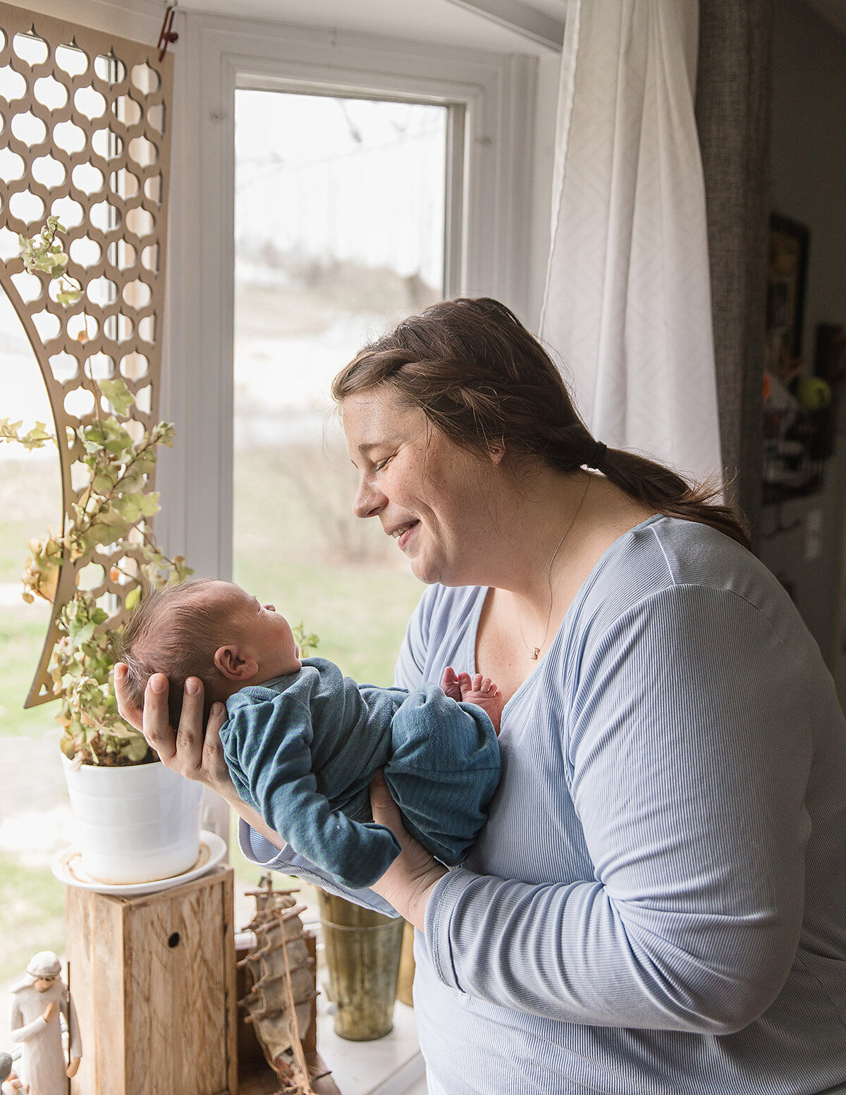 Smiling Mom Laughs at Newborn in Front of Home Window