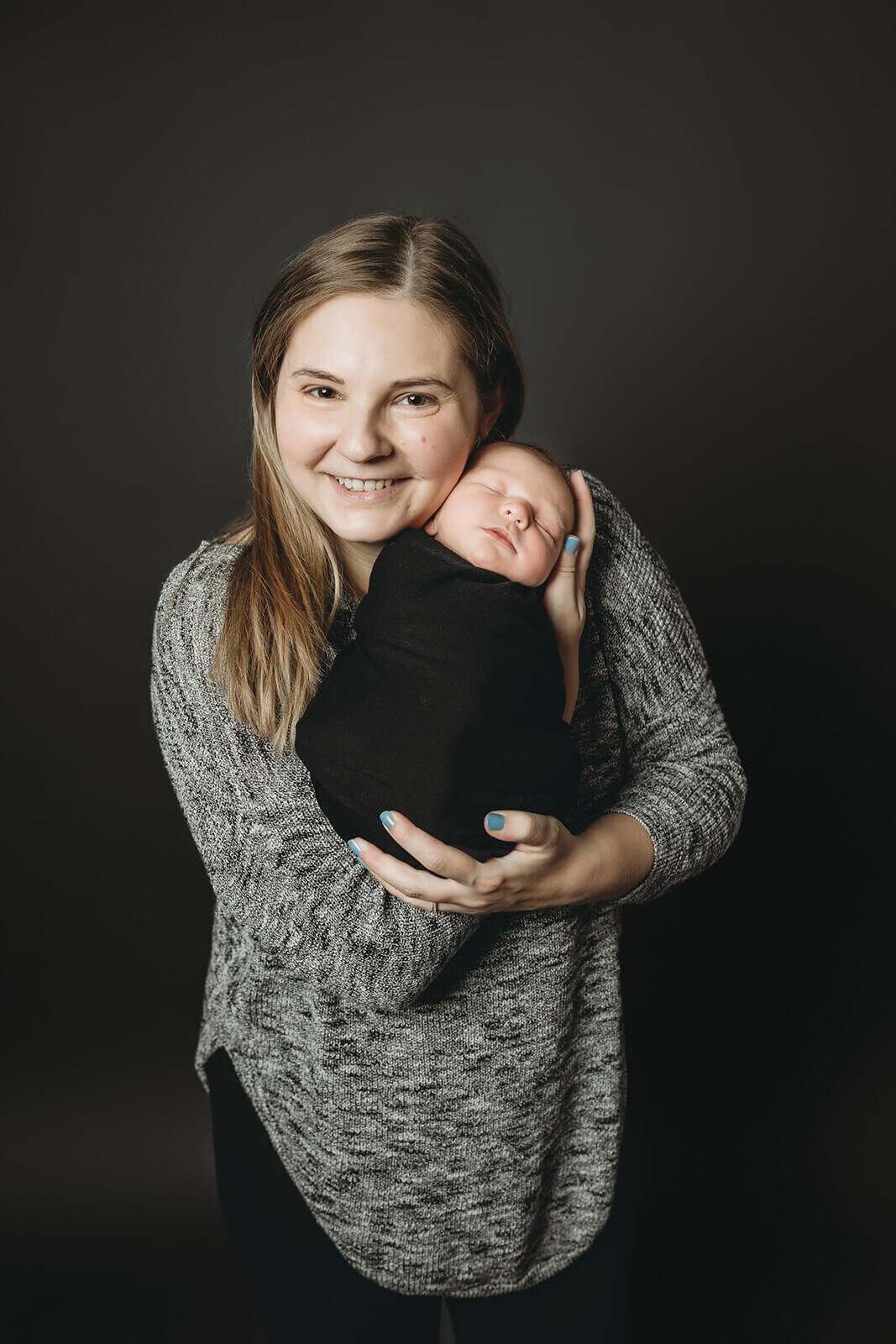 newborn baby boy swaddled in black being held by his mom in a dark background for parent portraits in york newborn photos 