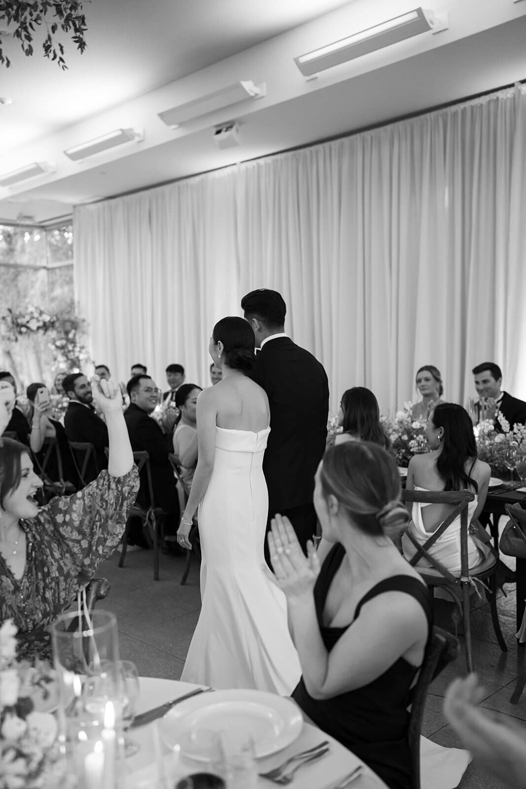 Bride and groom walking hand-in-hand as they enter their wedding reception venue at the Aspen Meadows Resort, surrounded by friends and family.