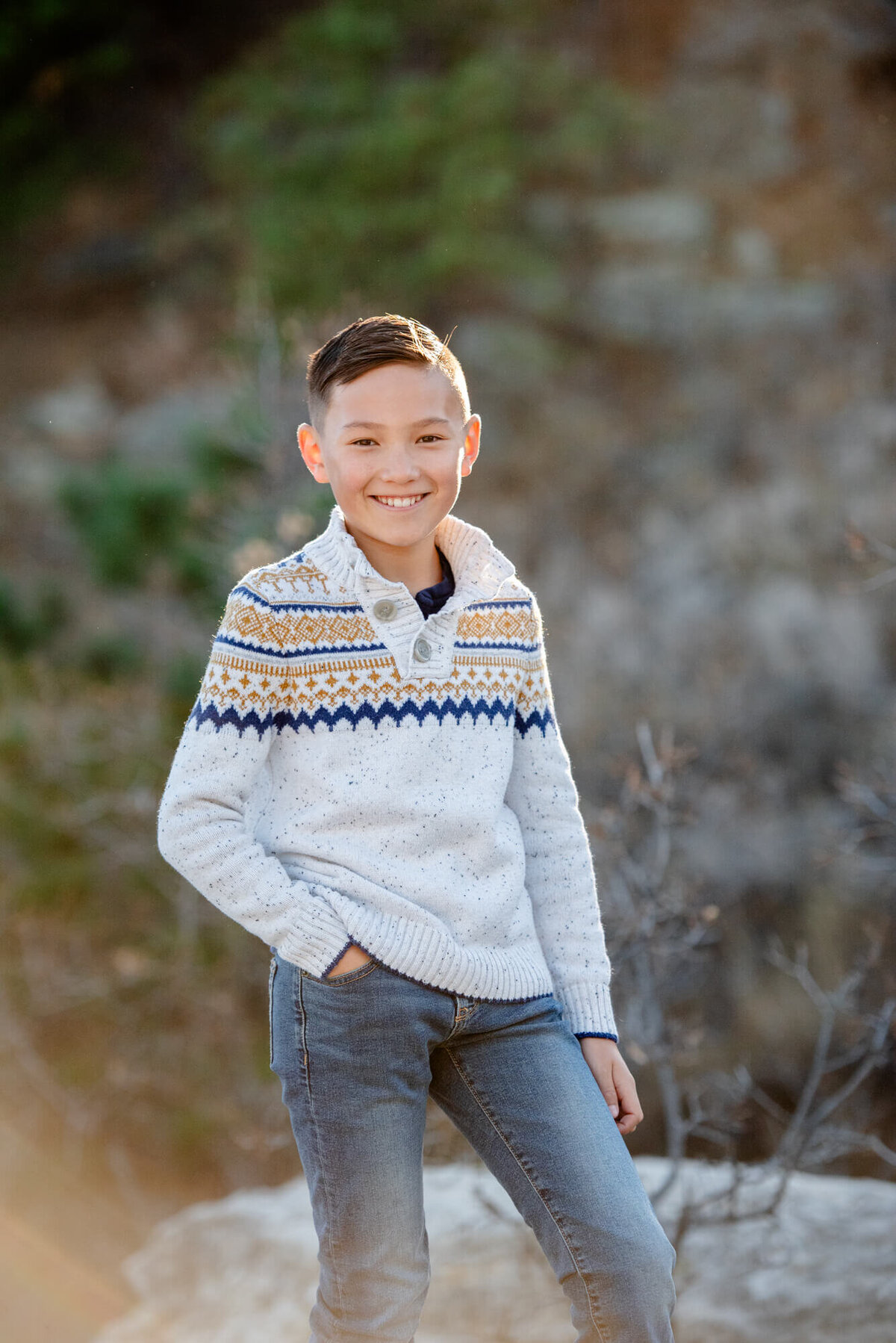 A young boy stands on a trail with a hand in his pocket in a white sweater