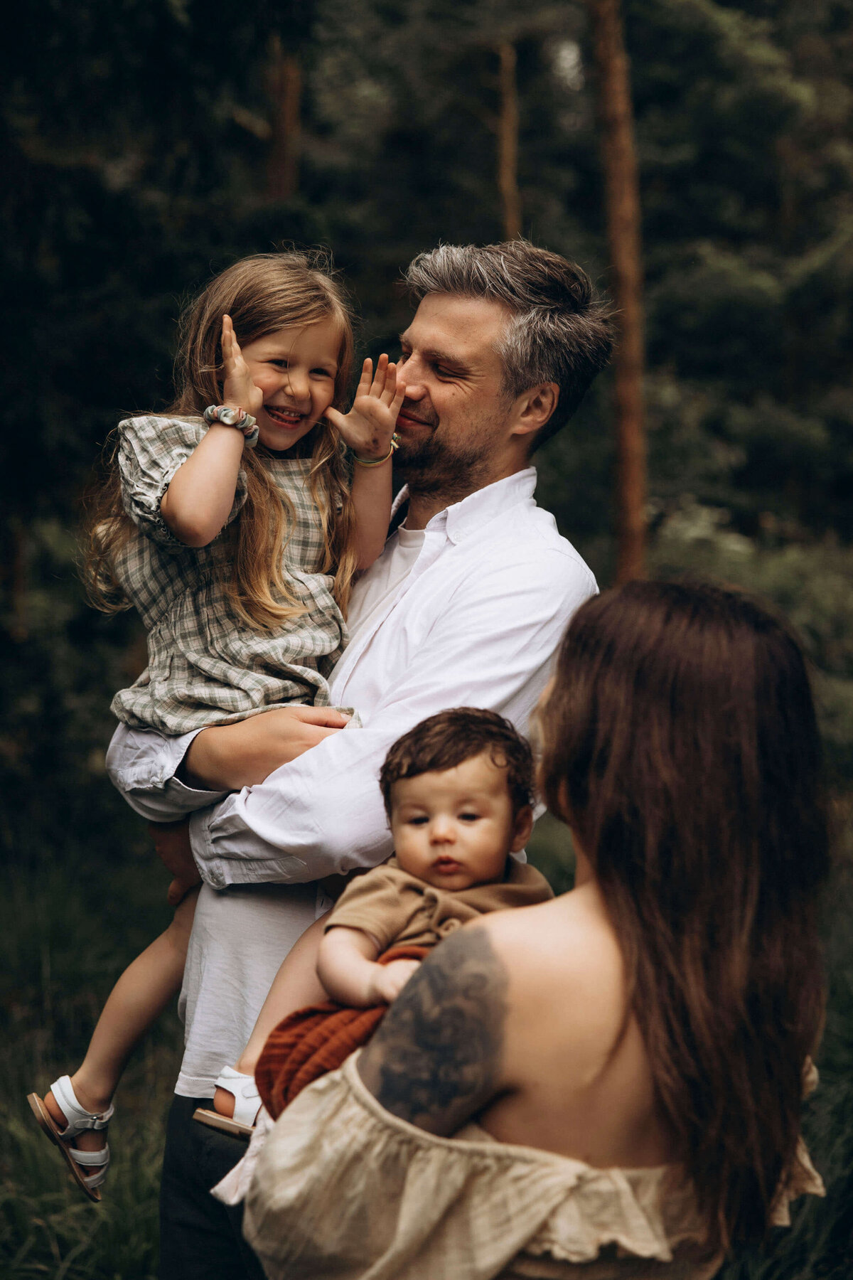 family of four with dad holding his smiling daughter and mom holding her baby