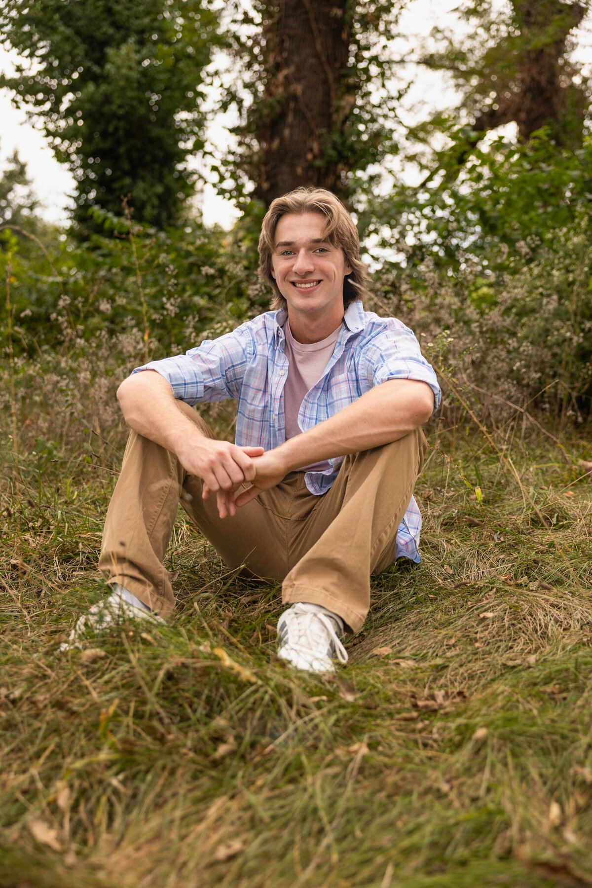 A senior guy sitting on the grass with arms on knees in Lawrence, KS