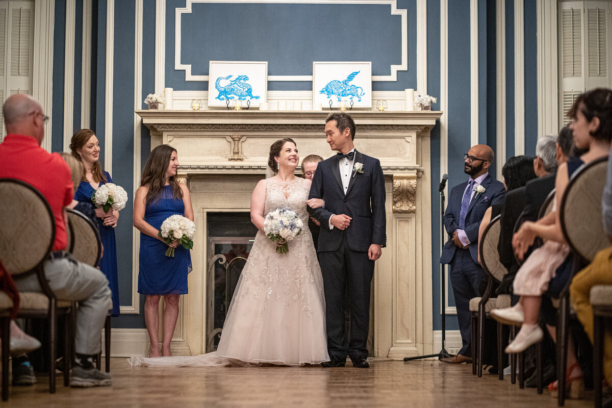 Bride and groom smile at each other and link arms as they walk back down the aisle as a married couple