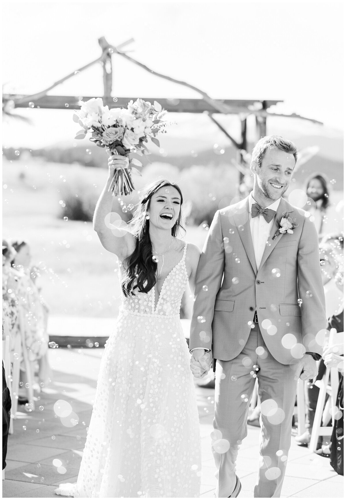 Bubbles fly in front of a bride and groom as they exit their ceremony with guests surrounding them at a Denver wedding Venue