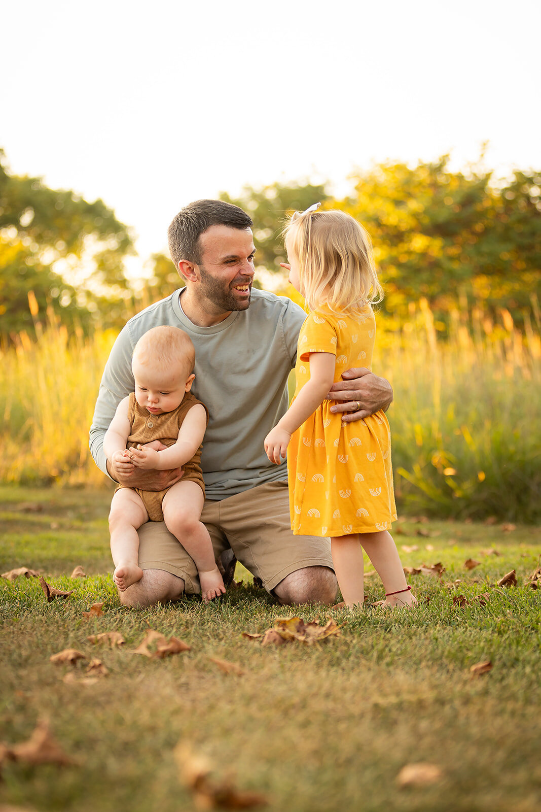 dad laughing with daughter and holding son in field