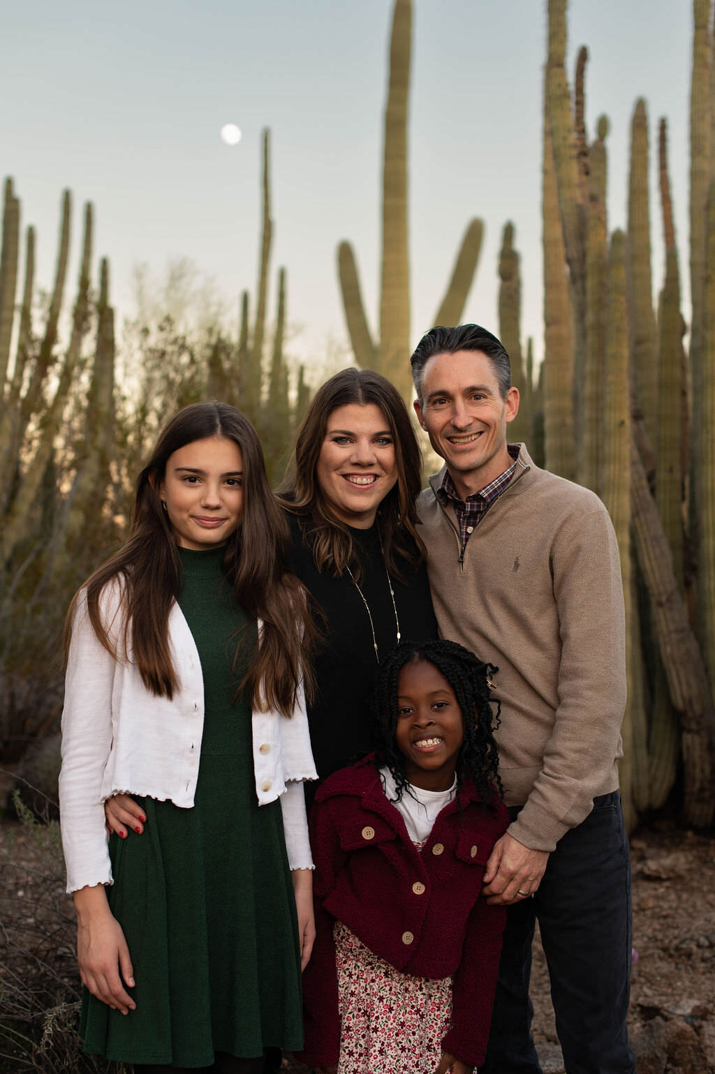 A family standing together smiling with desert plants behind them.