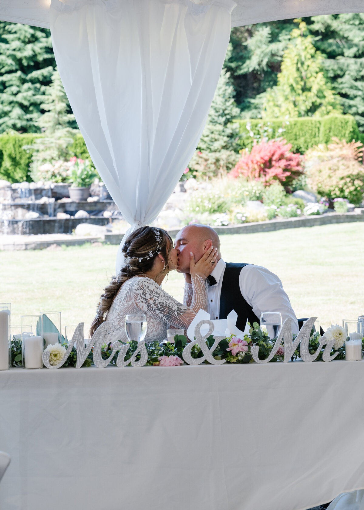 wedding couple kiss at head table under white tent
