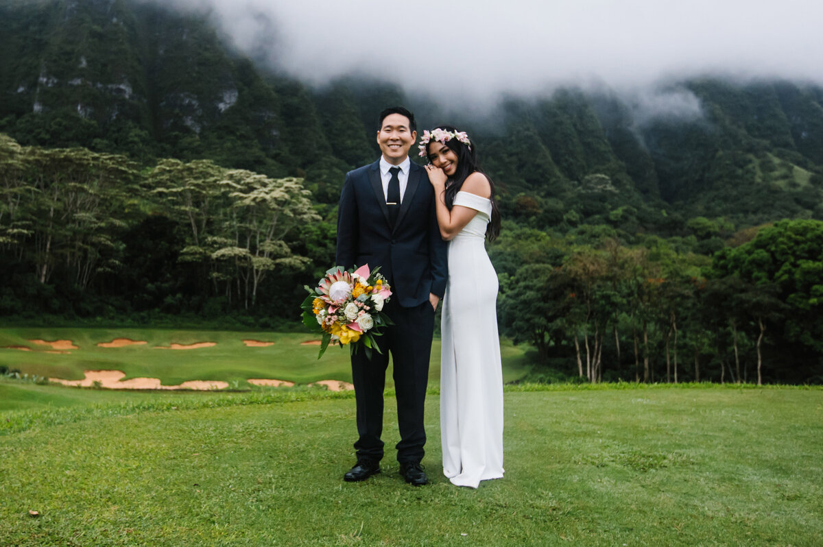 bride and groom look at camera with mountains in background in hawaii