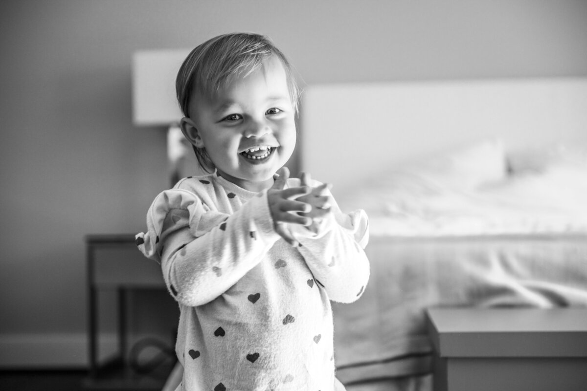 Toddler clapping hands in bedroom looking at camera black and white