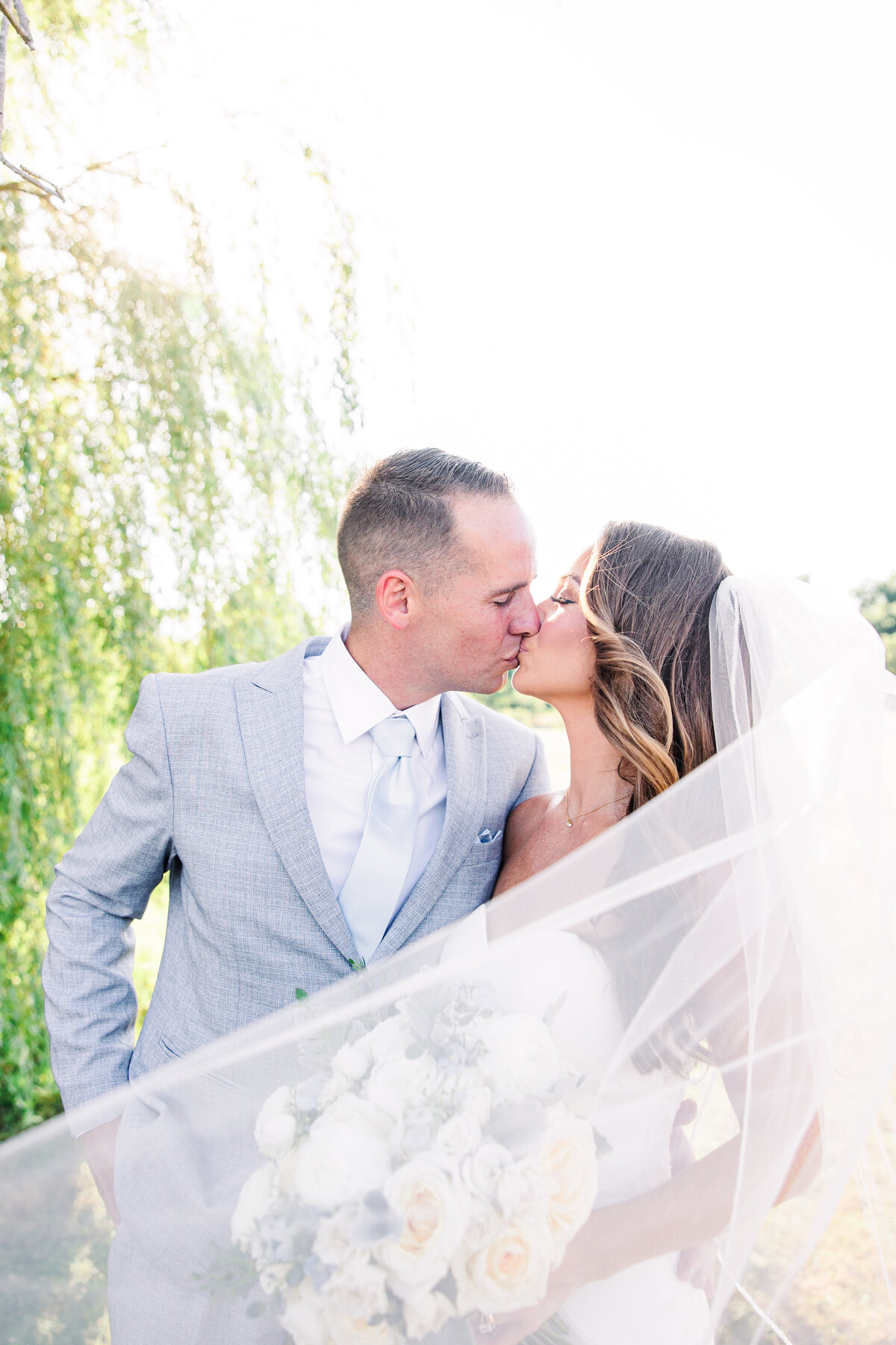 Bride and groom kissing with the veil blowing in front of them representing the best Boston wedding photographer