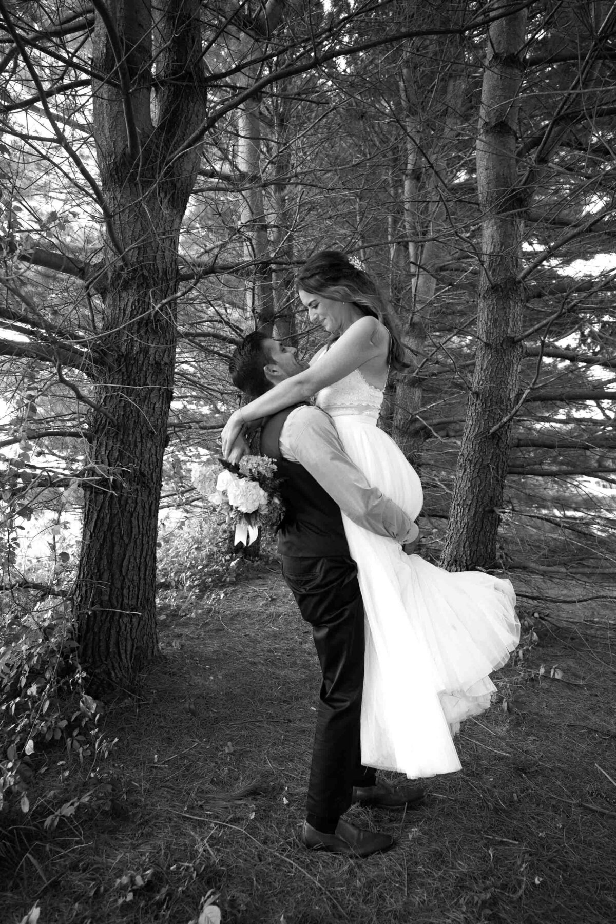 groom lifting his bride up during wedding day portraits in the woods next to a farm in Pennsylvania 