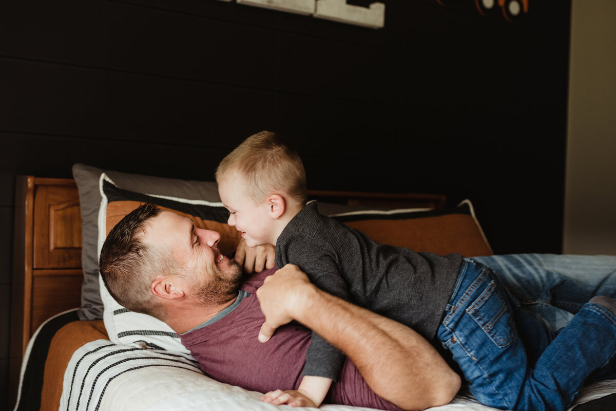 dad and toddler son playing on bed near St. Louis