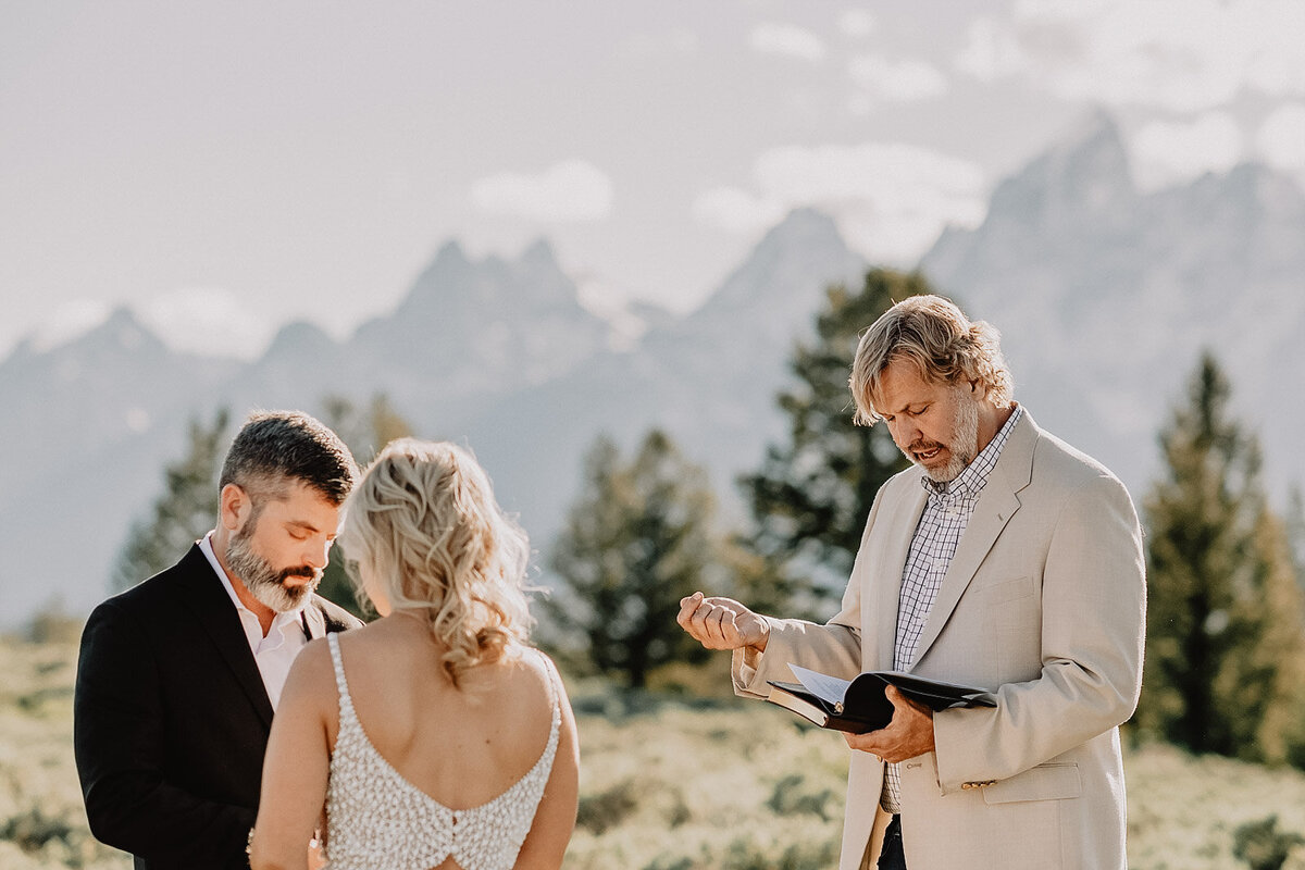 bride and groom standing with their officiant in the grand tetons for an outdoor wyoming elopement in a meadow next to the mountains
