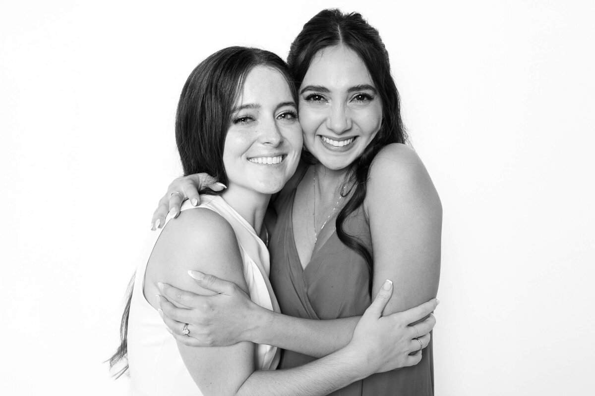 Two women smiling and embracing in a black and white photo booth portrait by Monochrome Portraits, a modern Phoenix photo booth.