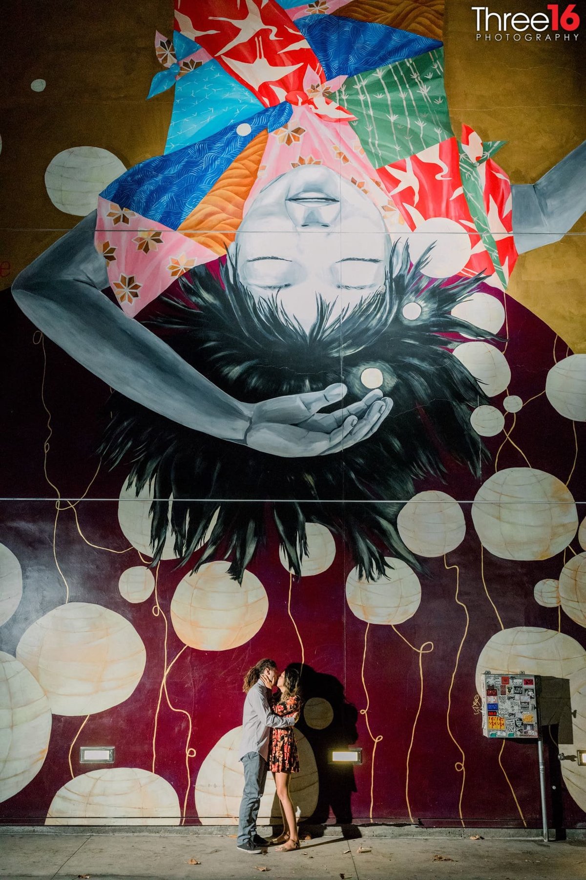 Engaged couple kiss in front of a large colorful mural at The Geffen