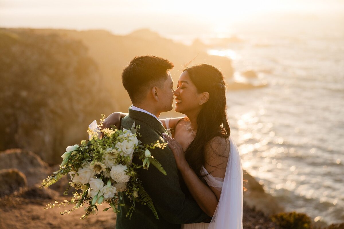 During sunset, the bride and groom embrace with the ocean in the background.