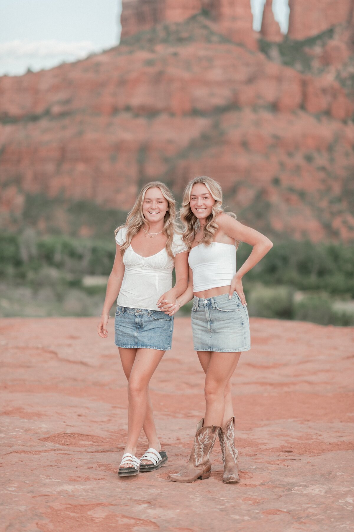 two senior girls standing on a rock with cathedral rock behind them holding hands