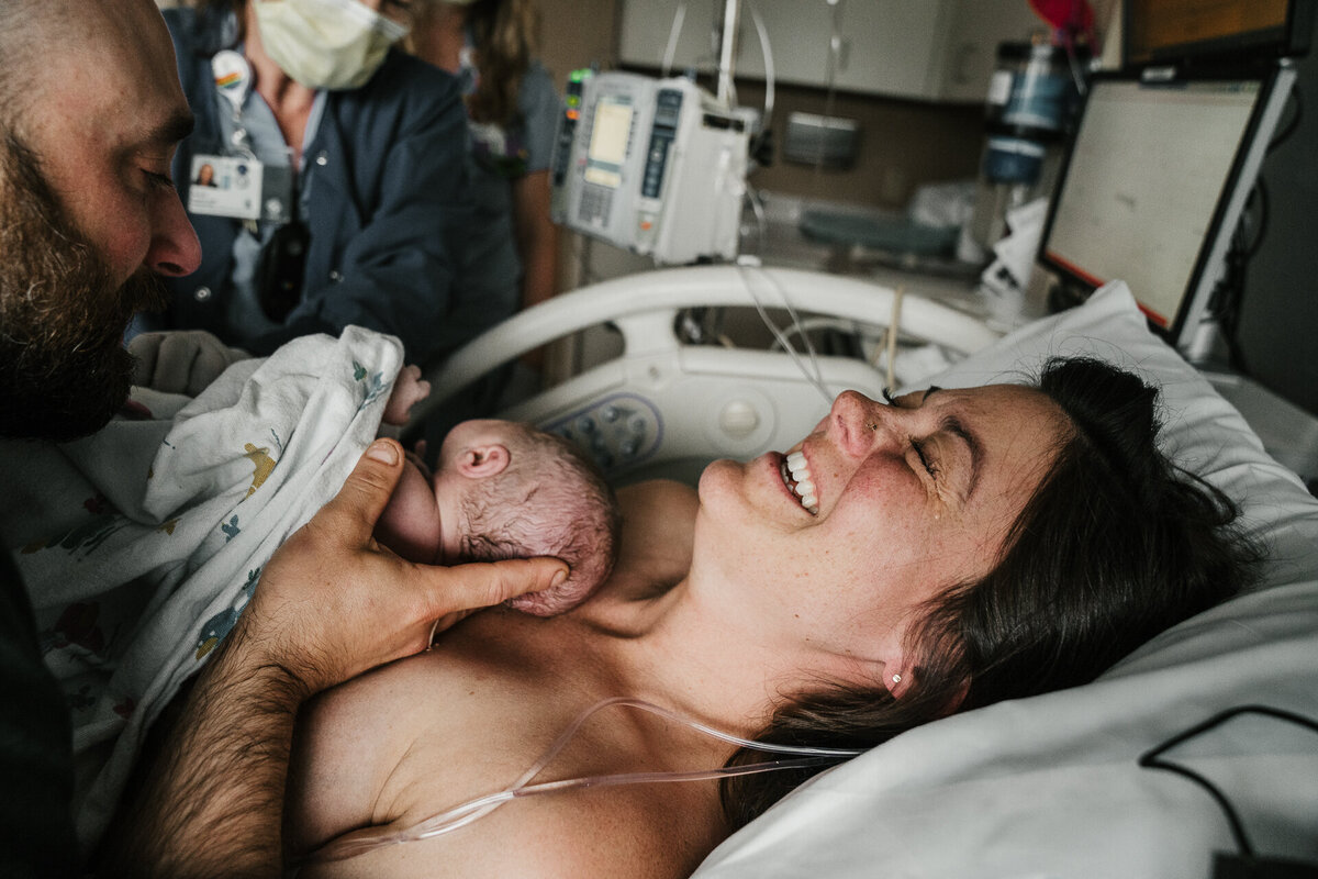 Mother cries holding newborn in the hospital next to her husband