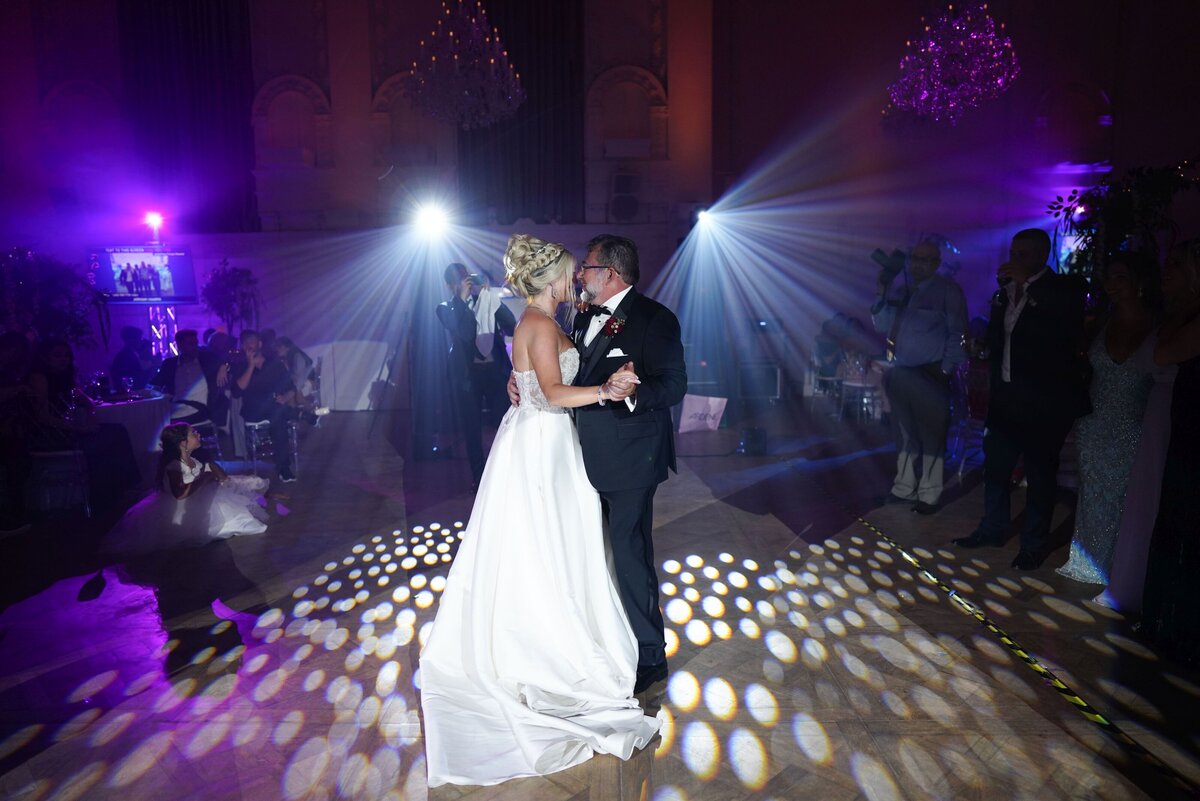 The bride and her father enjoy a heartfelt dance at the wedding reception, surrounded by the joyous atmosphere of the celebration. The tender moment highlights their strong bond and the special memories being created on this significant day.