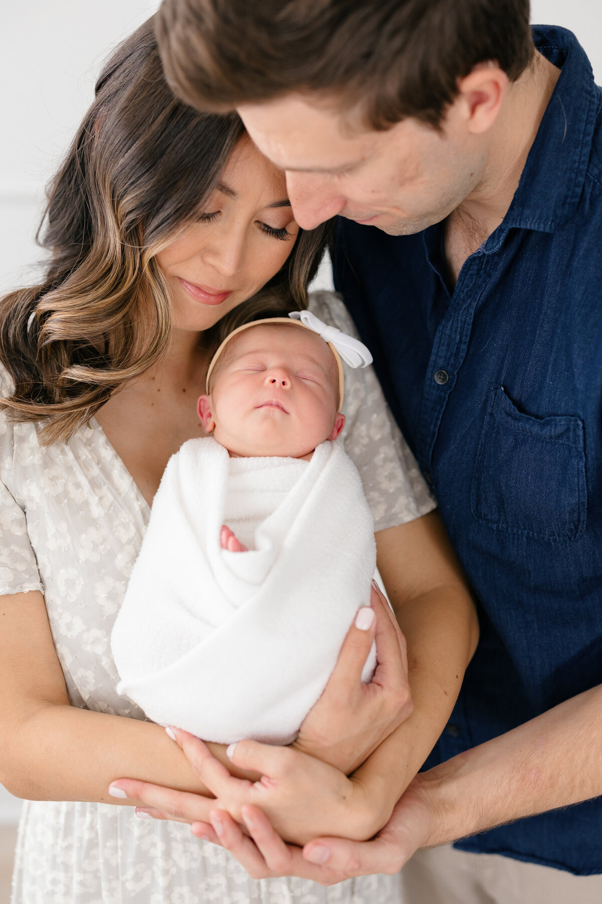 New parents snuggling and holding their sleeping baby girl who is swaddled in a white wrap