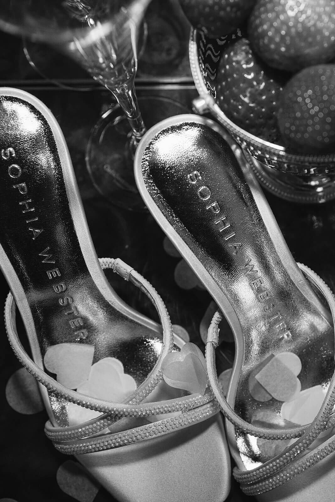 a pair of Sophia Webster wedding shoes with confetti over them next to a bowl of strawberries.