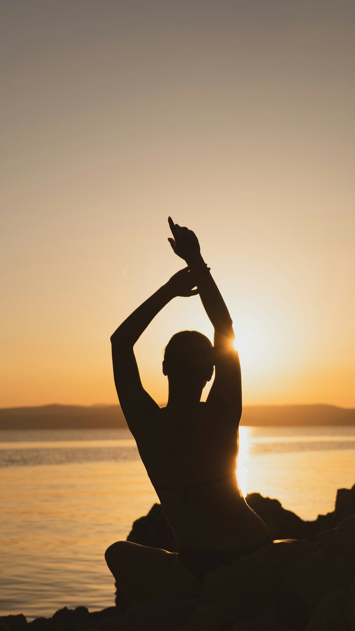 A silhouette of a woman stretching at sunset with a lake in the background. 
