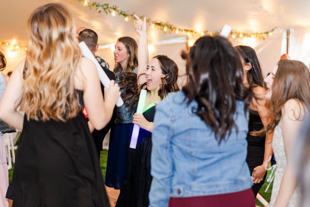 Guests dance during a wedding ceremony under a white wedding tent with glowing lights around them