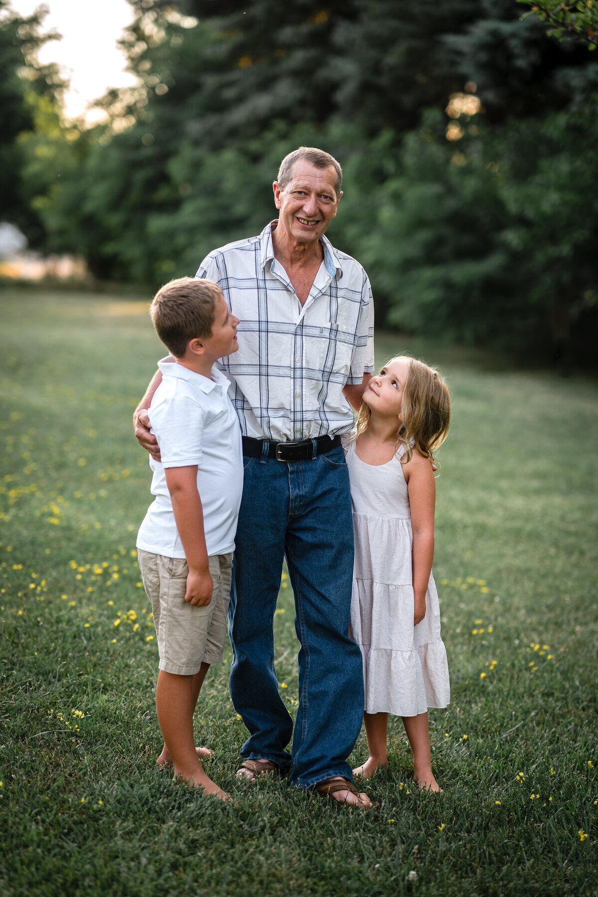 A grandfather in a plaid shirt is holding his two grandchildren as they look up at him.