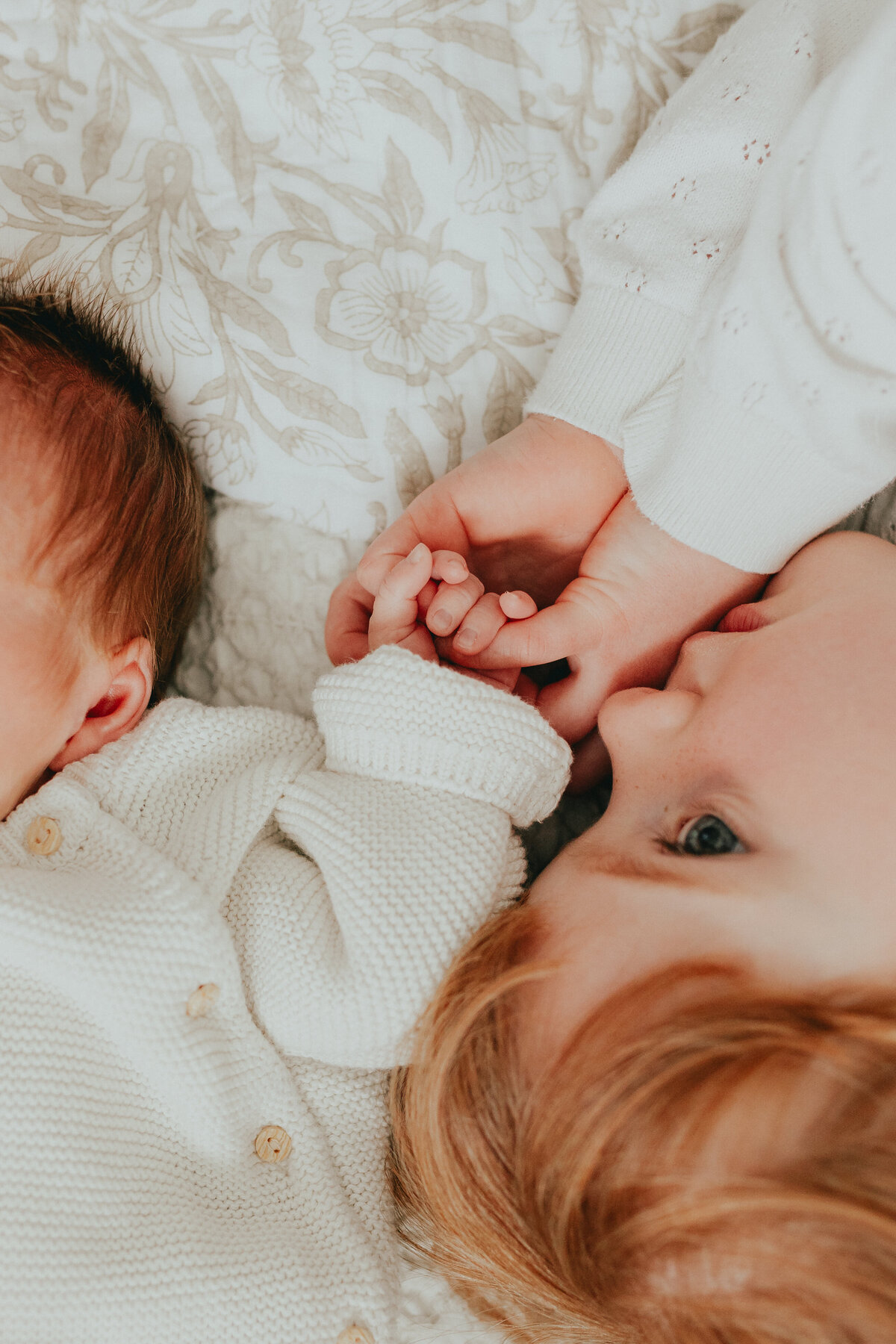 Close up photo of a girl and her baby brother laying on the bed where the girl is holding the baby's hand taken by a Langley Family Photogrpher