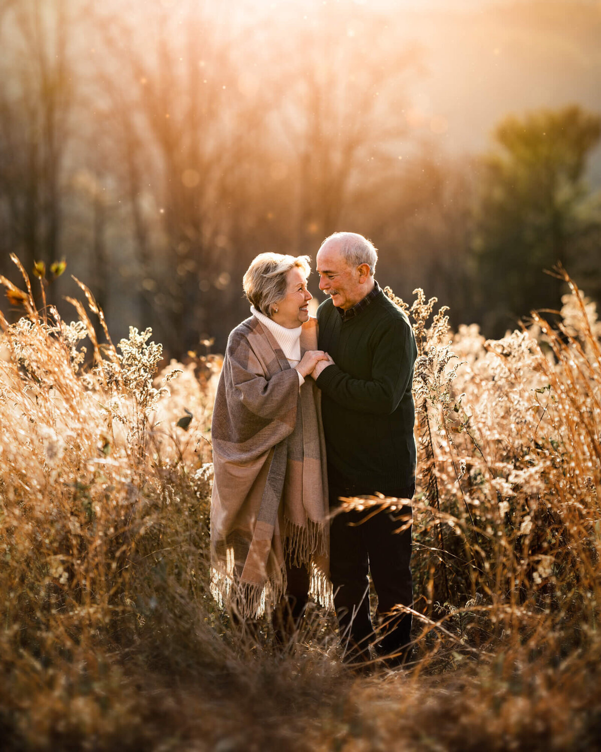 A couple in their golden years snuggling and laughing in tall yelllow grass at sunset