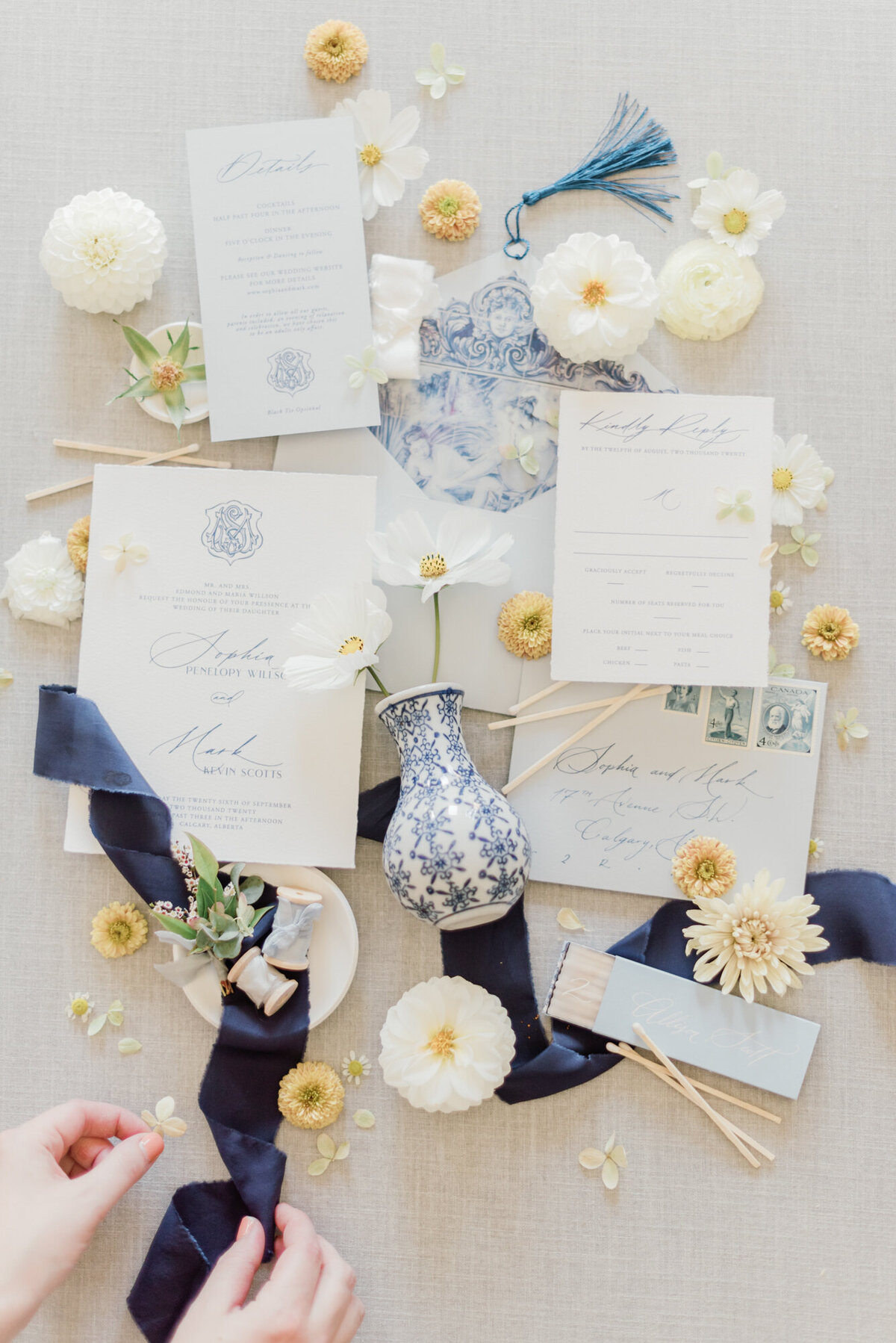 Wedding Stationery and details flatlay, styled by Wedding Stylist Rebekah Bronte, featuring blue and white details, navy ribbon, and yellow and white florals. 