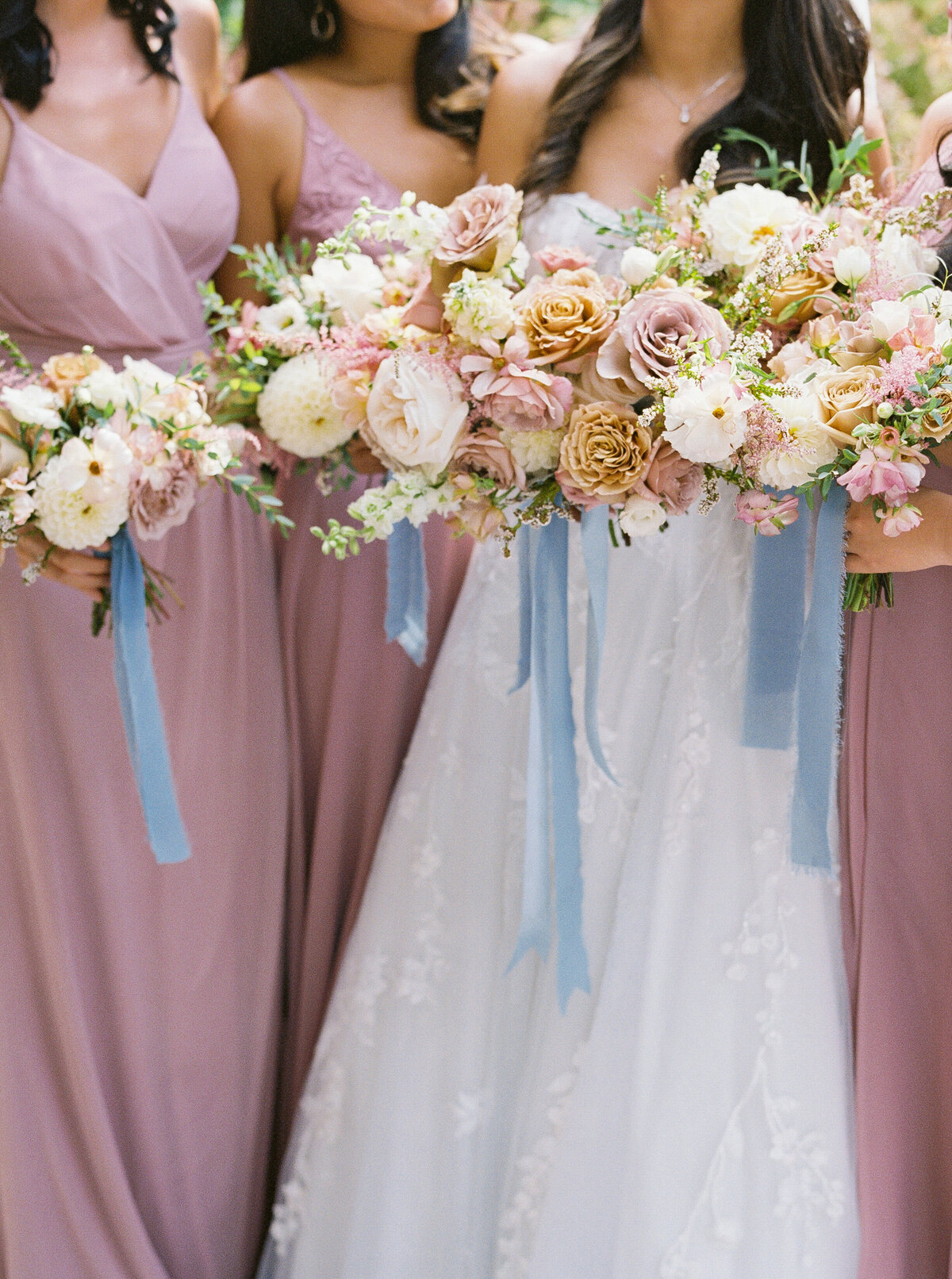 Bridesmaids holding bouquets in soft floral tones with blue ribbon accents at Castle Ladyhawke.