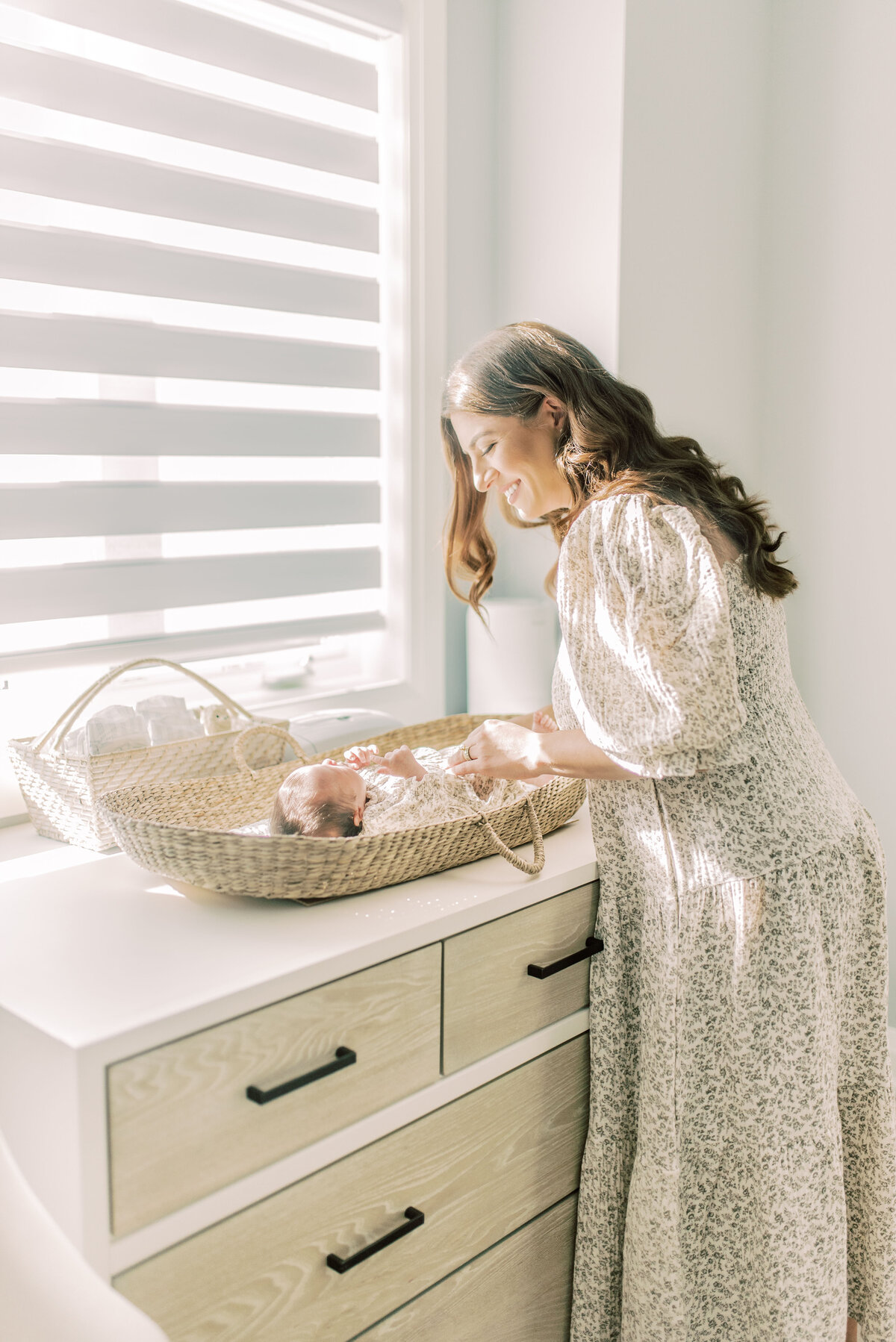 Alyssa, a new mother and event planner, smiling down at her baby in a Moses basket – soft sunlight and maternal warmth