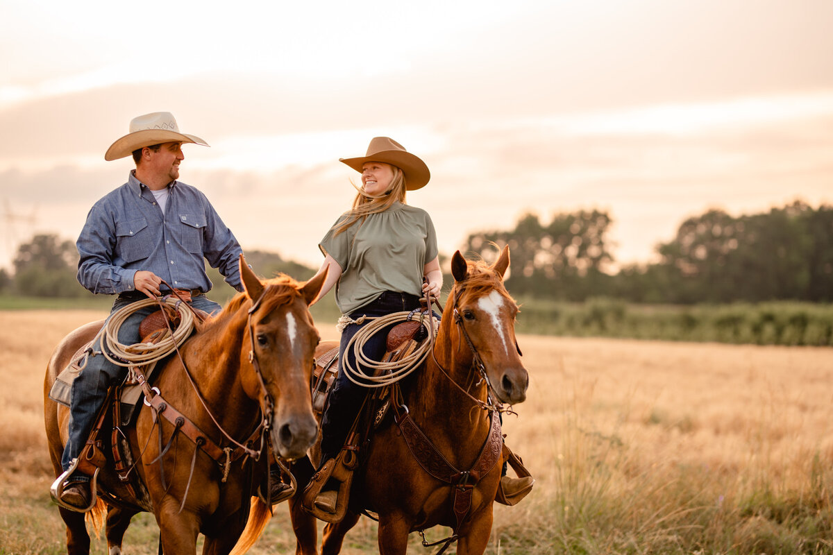 Photo of cowboy couple riding their roping horses through a field.