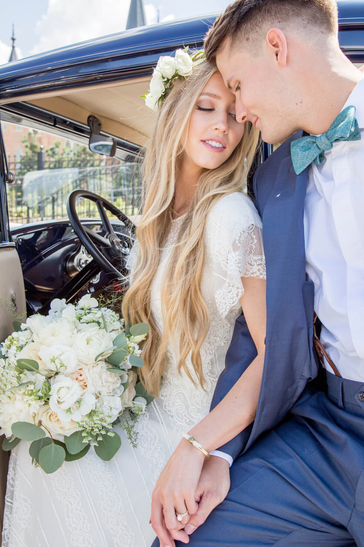 a bride and groom holding hands and leaning into each other in front of a blue vintage car