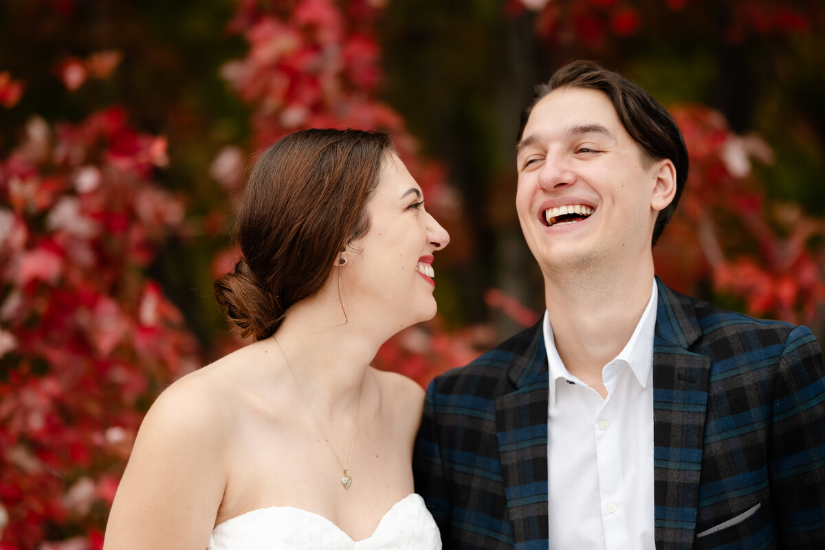 A couple laugh in front of a red colored tree