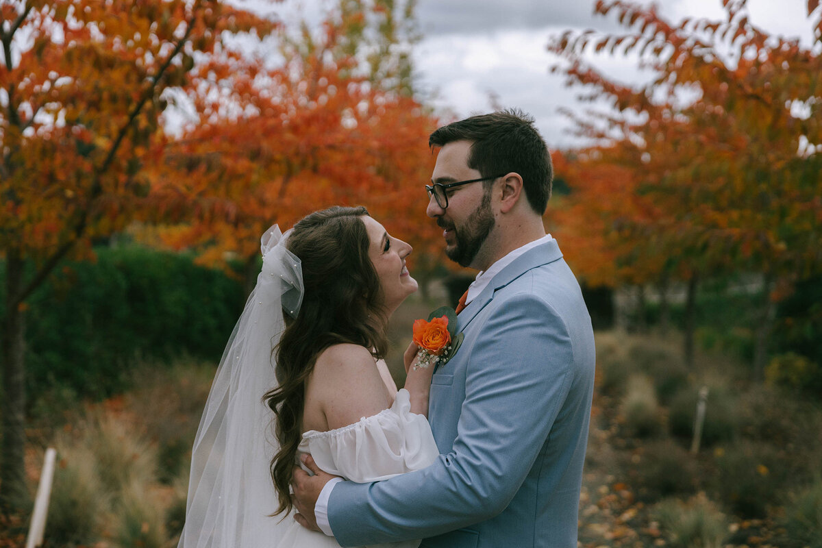A bride and groom embrace and smile at each other at a fall outdoor wedding.