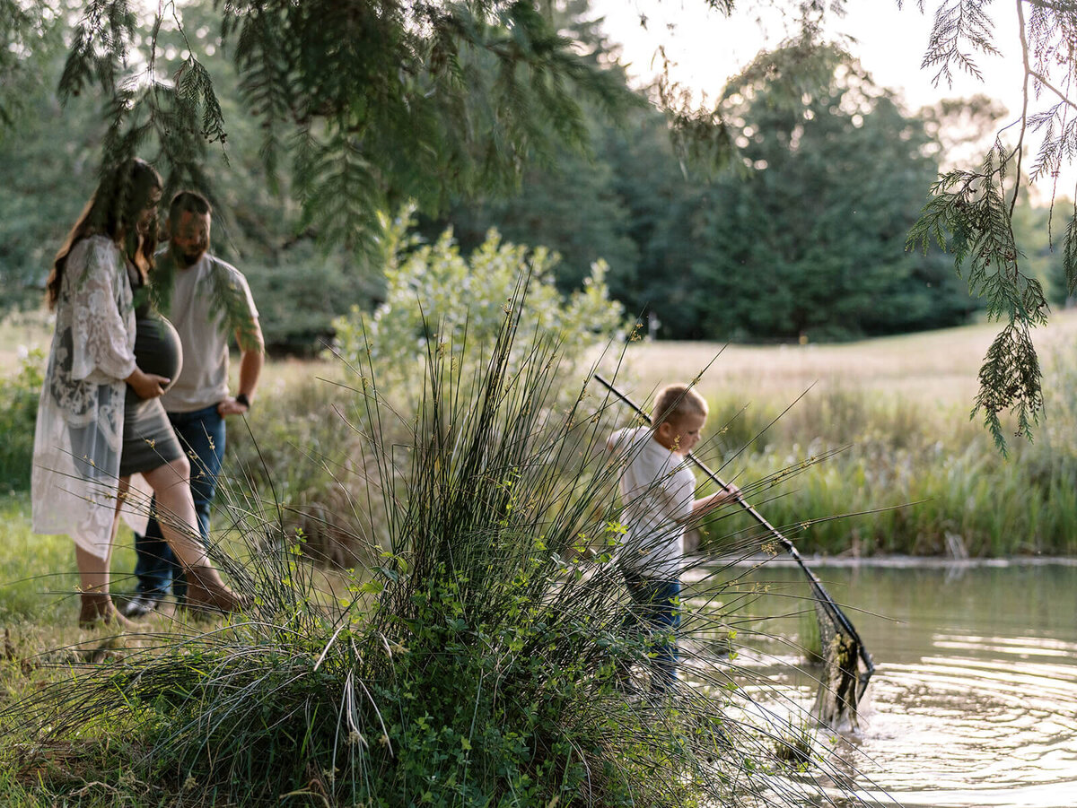 A boy fishes with a net while his parents watch.