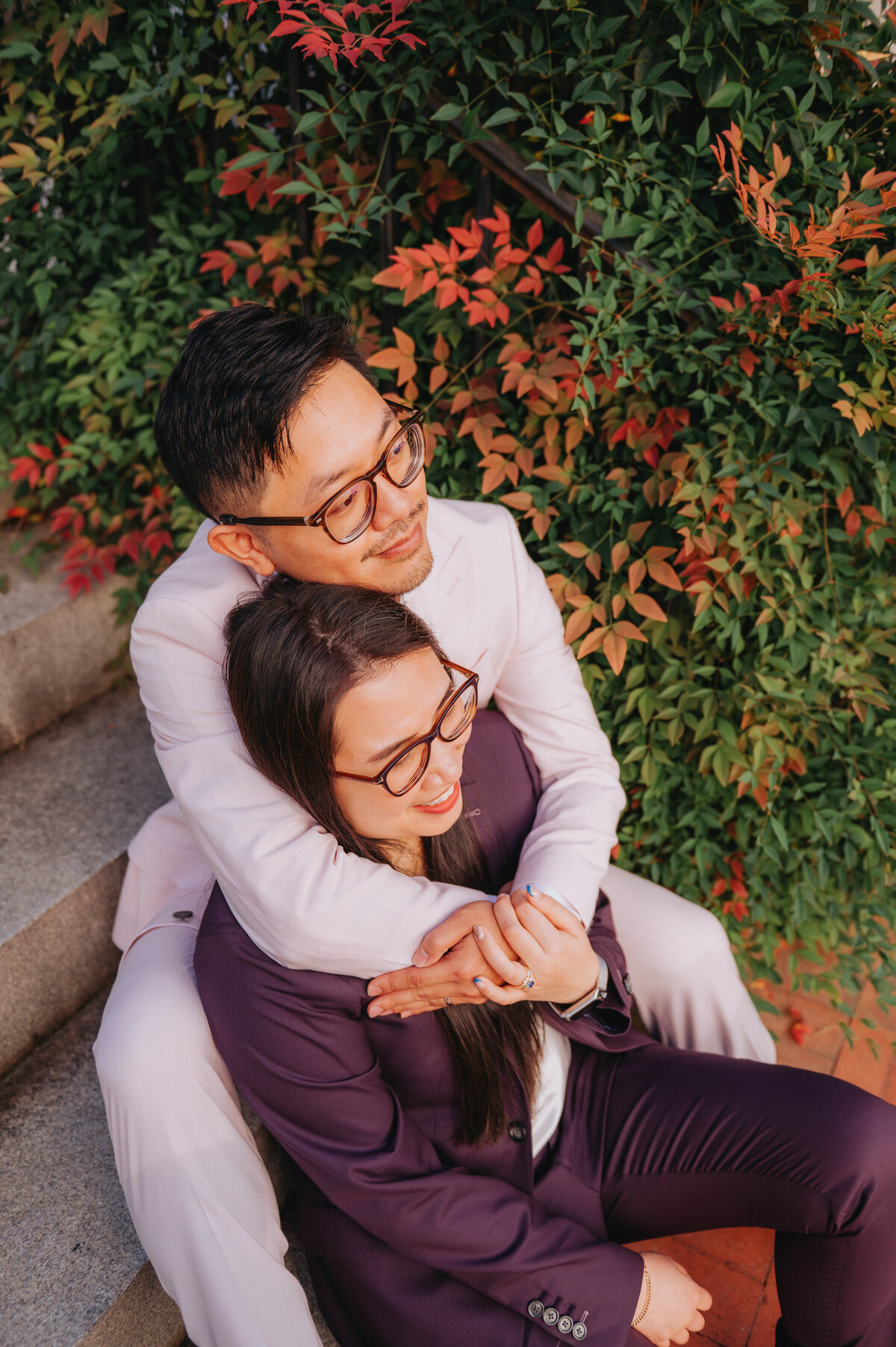A couple hugs one another next to fall foliage while sitting on steps