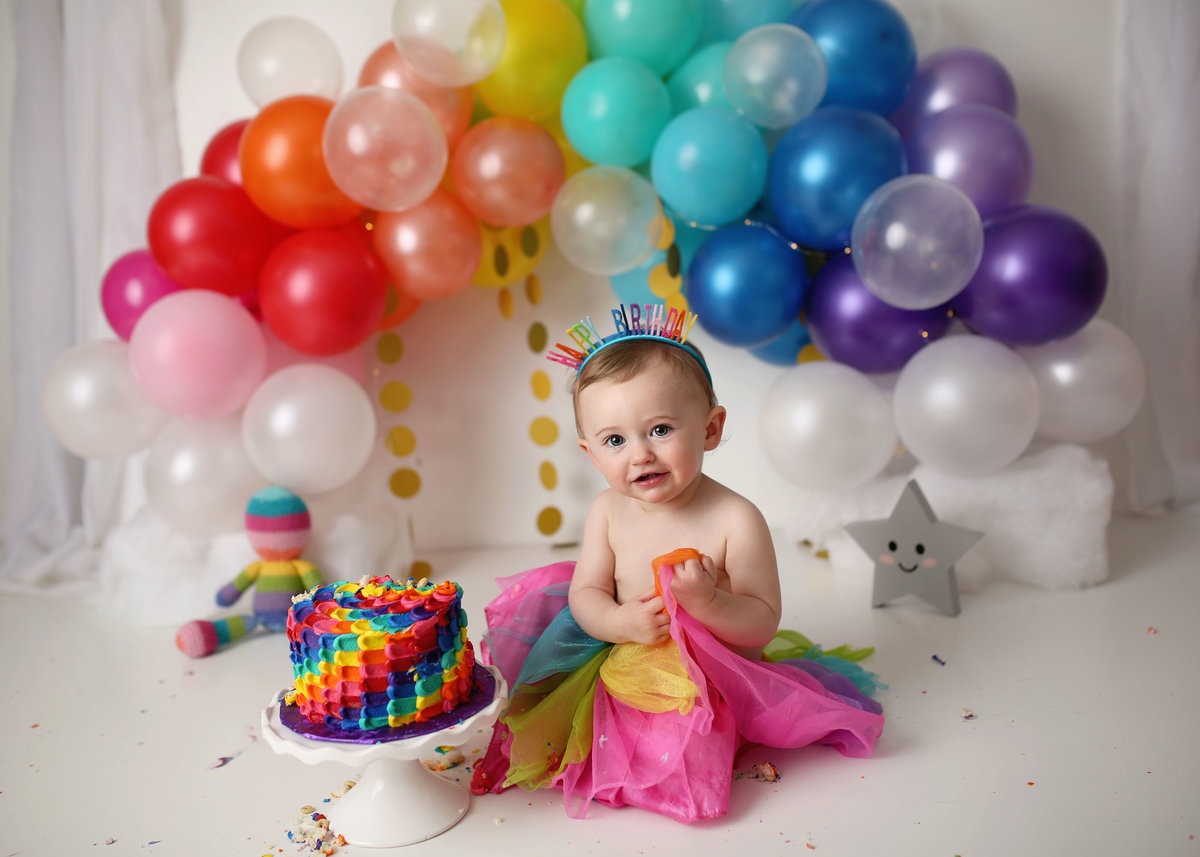 baby girl with rainbow cake and rainbow arch of balloons