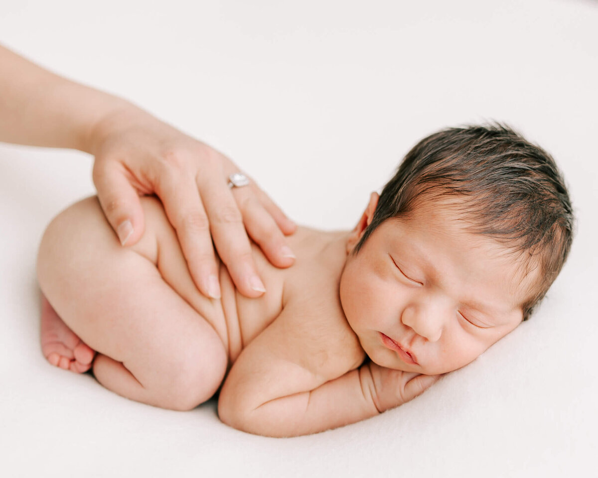 portrait of newborn boy sleeping with mom's hand on his back
