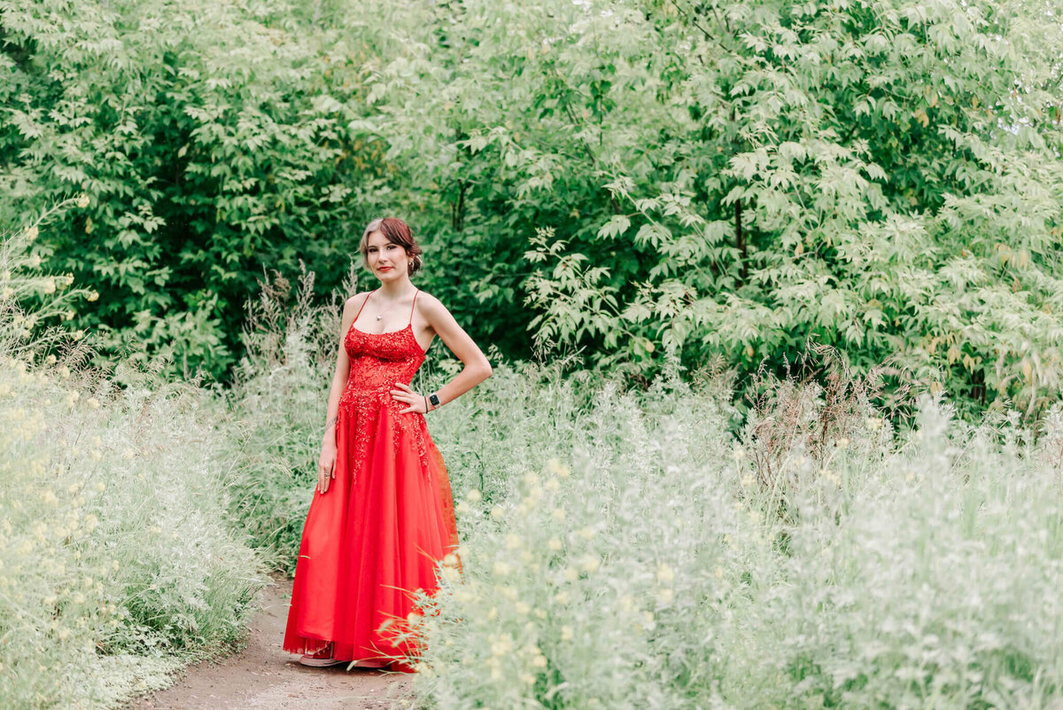 A full length shot of a girl in a red dress standing on a dirt path in Saskatoon. 