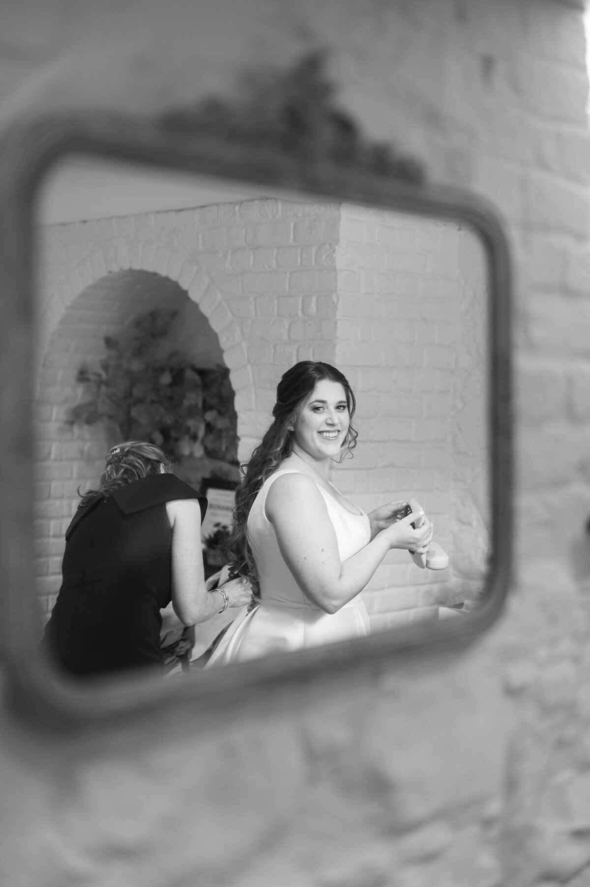 The reflection in a mirror of someone helping a bride put on a wedding dress