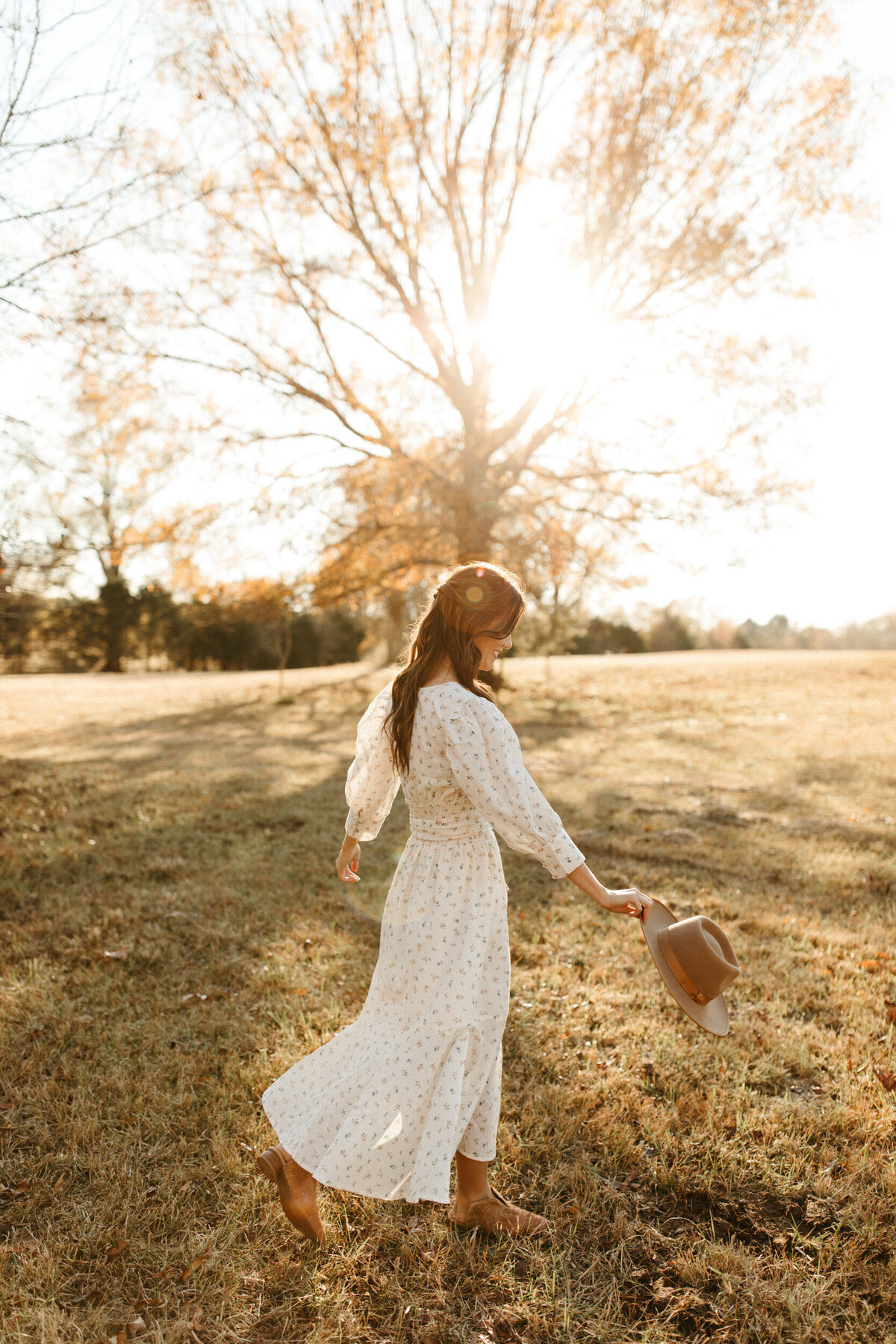 Boho senior girl twirling in a long white dress and holding a hat