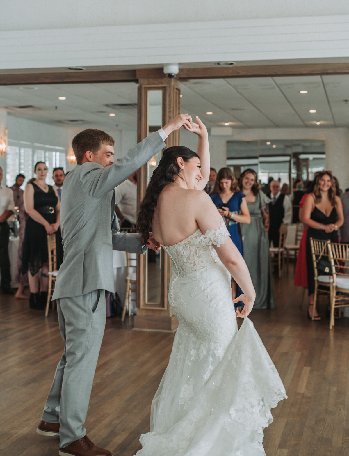 A newlywed couple joyfully dances on the wooden floor during their wedding reception at the Lesner Inn in Virginia Beach, surrounded by smiling guests, beautifully captured by Quinn Photography LLC.