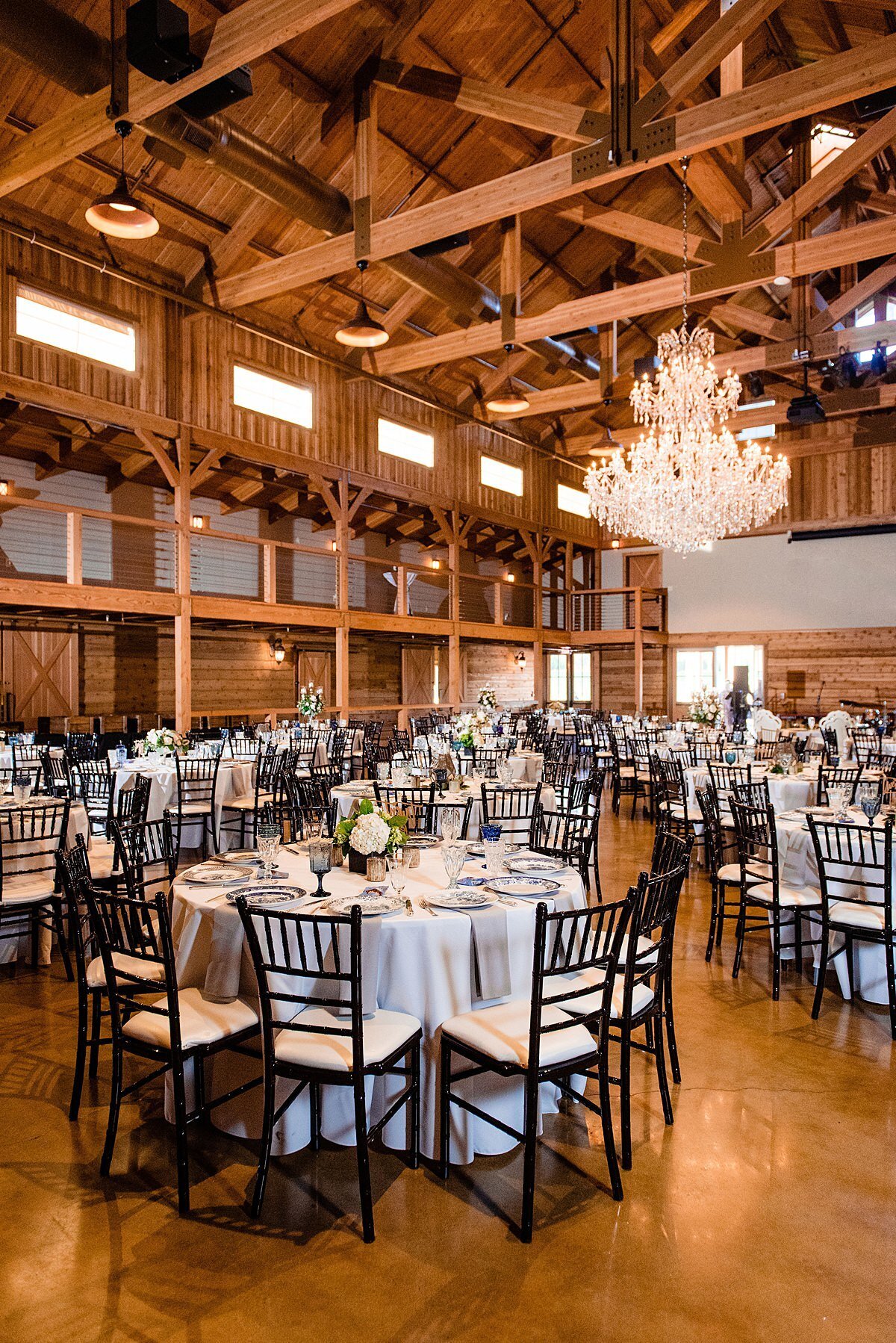 Large wedding reception with tables set with ivory table cloths, white and ivory floral centerpieces, mistmatchend blue vintage china, vintage blue water goblets and brown chiavari chairs at Sycamore Farms.