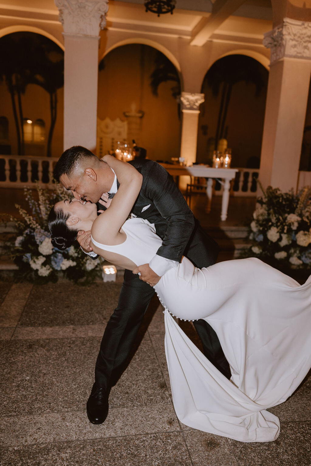 Groom dipping bride in front of european architecture at night during first dance
