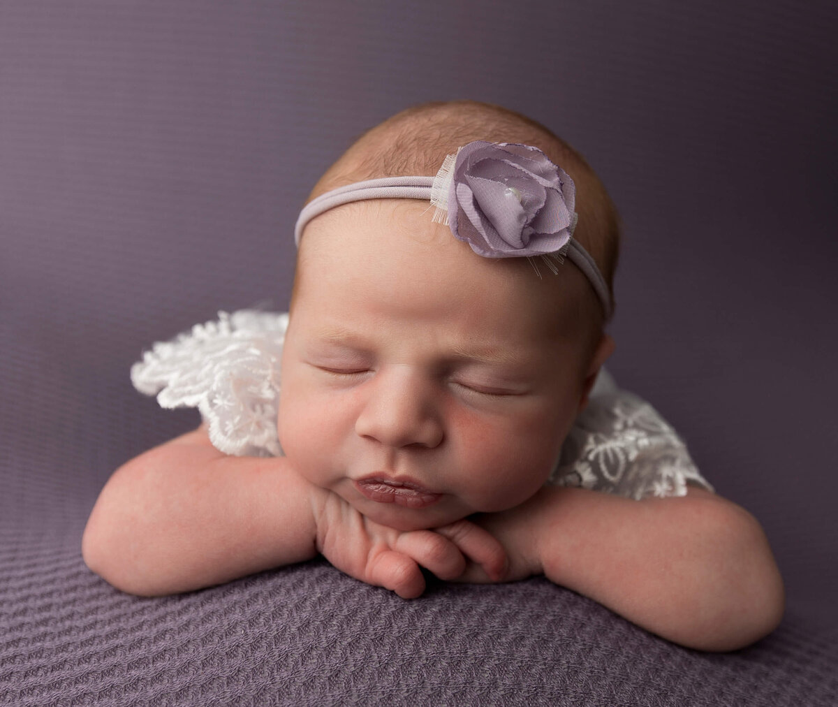 Newborn girl posed chin on hands on a purple backdrop in an Erie Pa photography studio