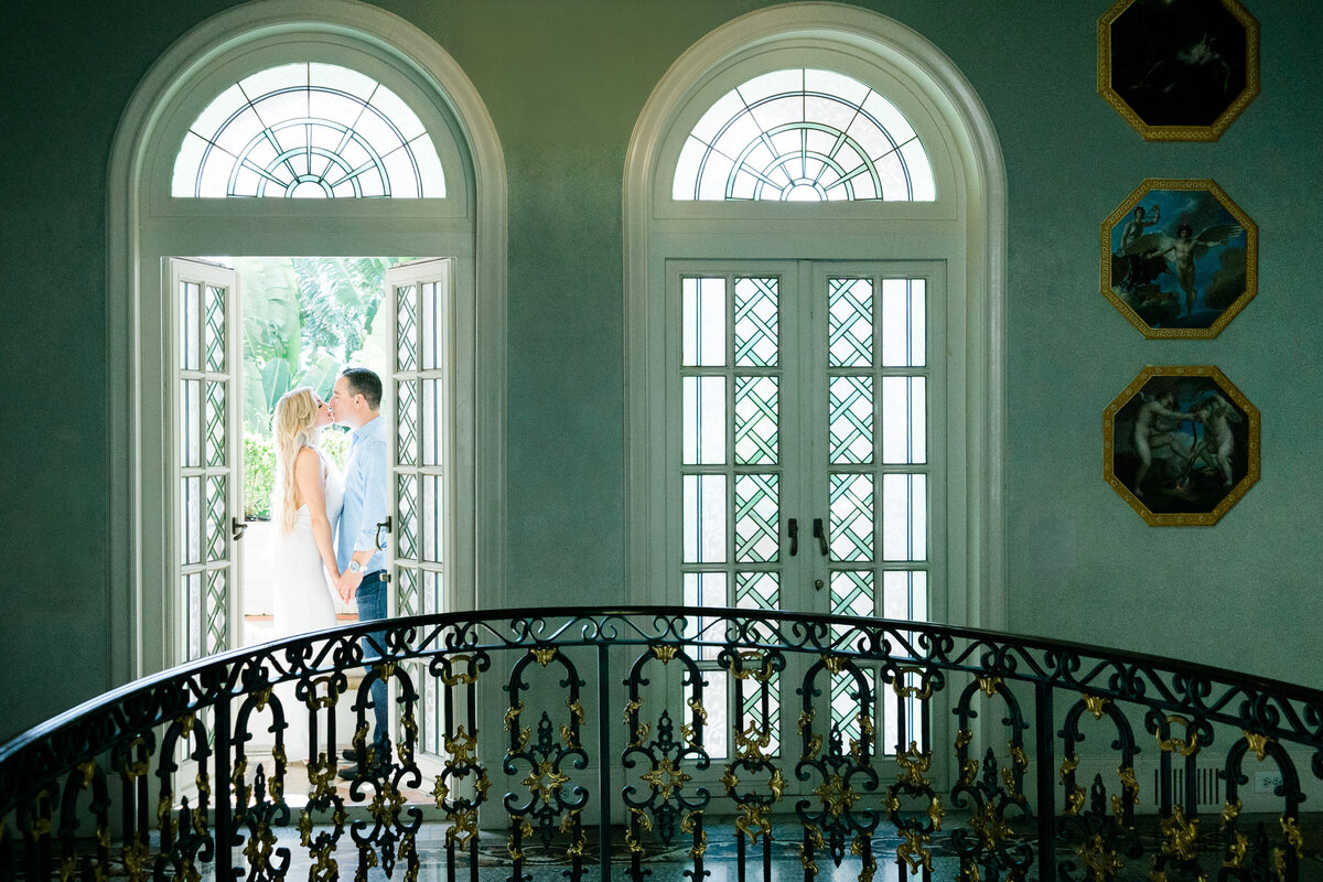 Romantic engagement portrait of a couple standing by French doors with elegant architecture, captured by Rodrigo Varela Photography in Miami, Florida. Classic and intimate setting for timeless photography.
