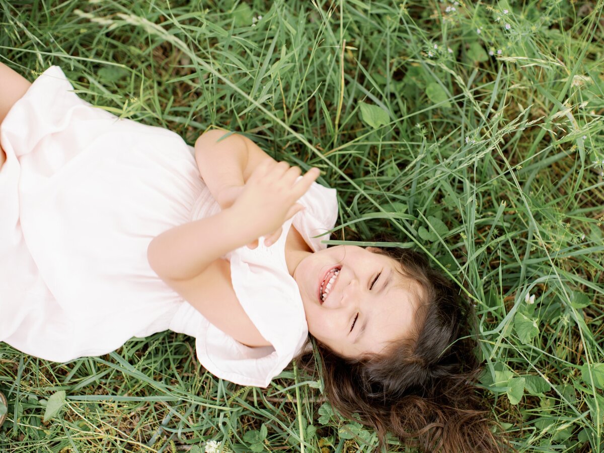 little girl laying down in grass laughing